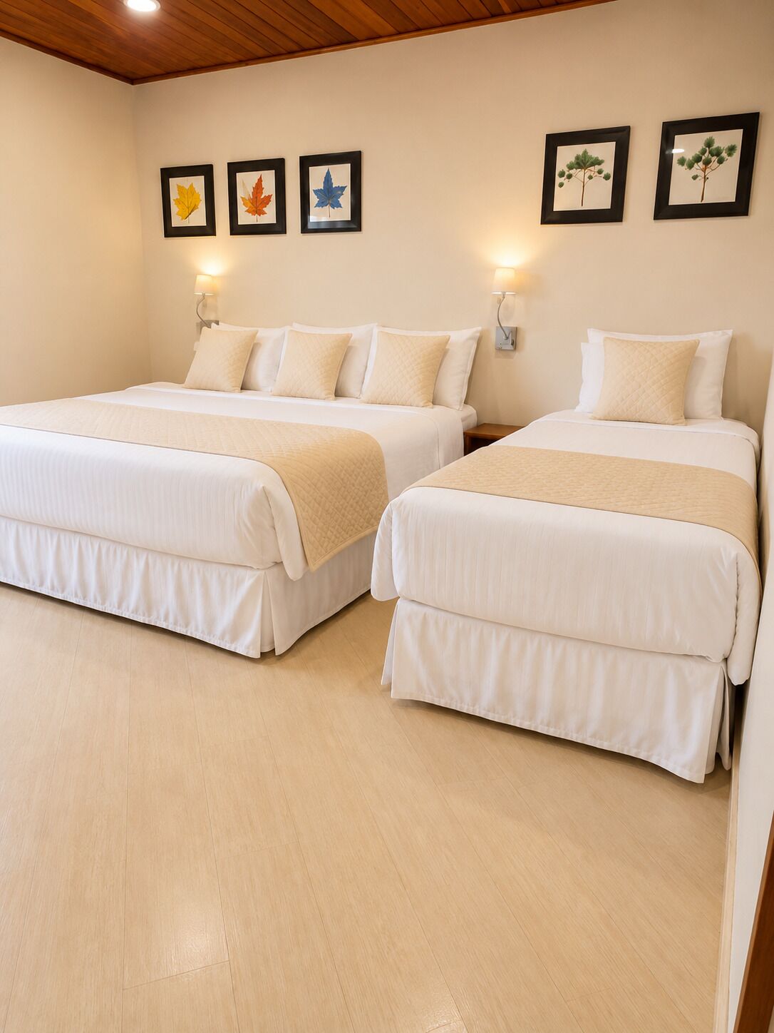 A hotel room with two beds, beige bedding, a wooden ceiling, and framed leaf artwork on the wall.