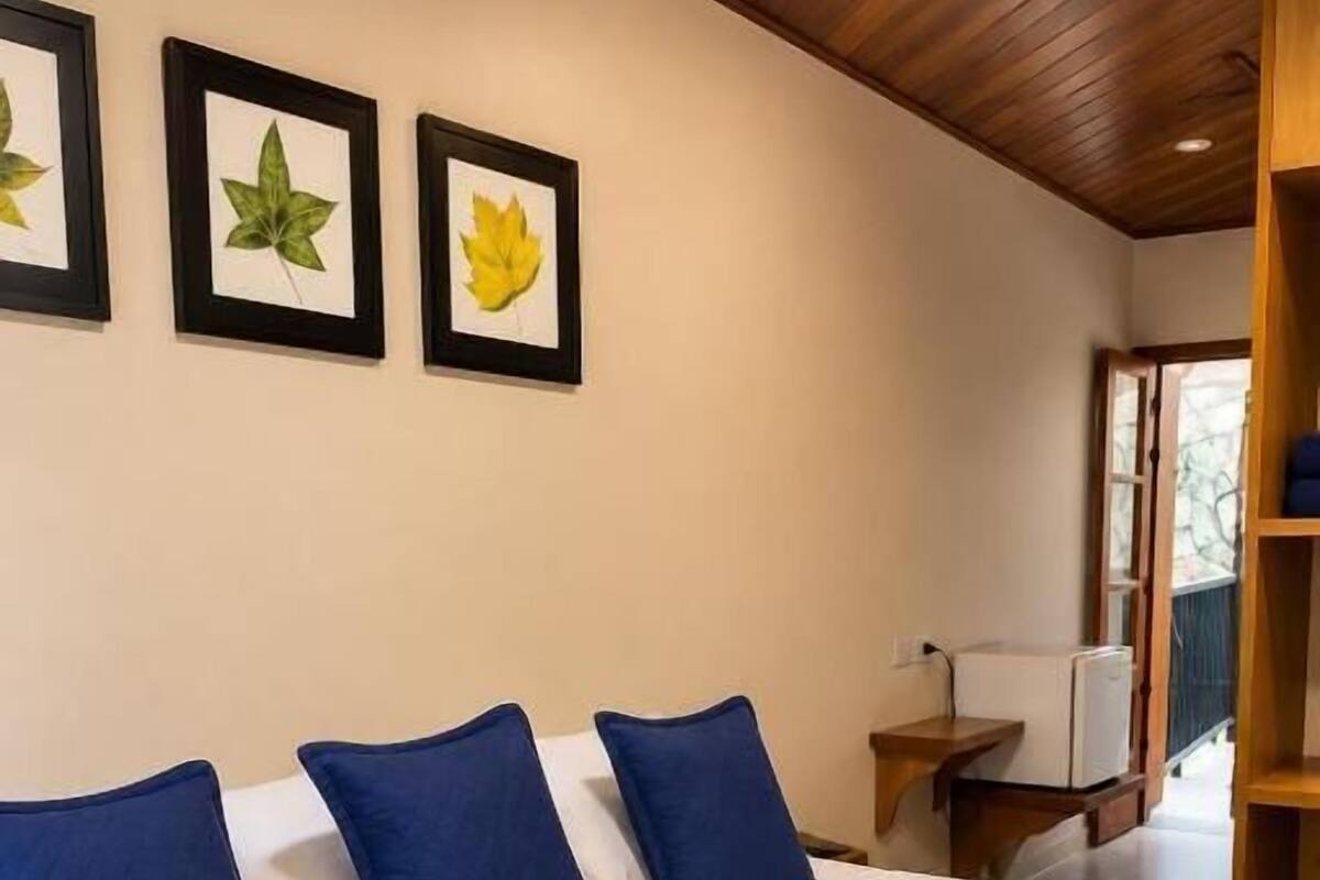 Ein Bett mit weißblauer Bettdecke, drei blaue Kissen und gerahmte Blätterbilder an der Wand.