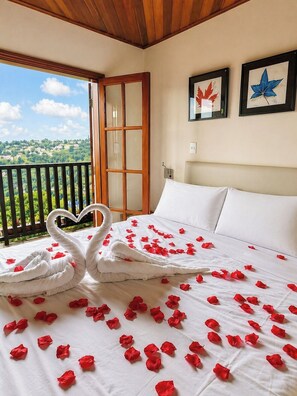 Quarto de hotel com varanda, cama com pétalas de rosa e duas folhas de bordo emolduradas na parede.