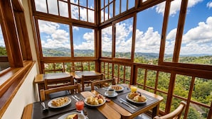A dining area with wooden furniture and large windows offering a scenic view. - Pousada Chateau Elegance (Campos do Jordão)