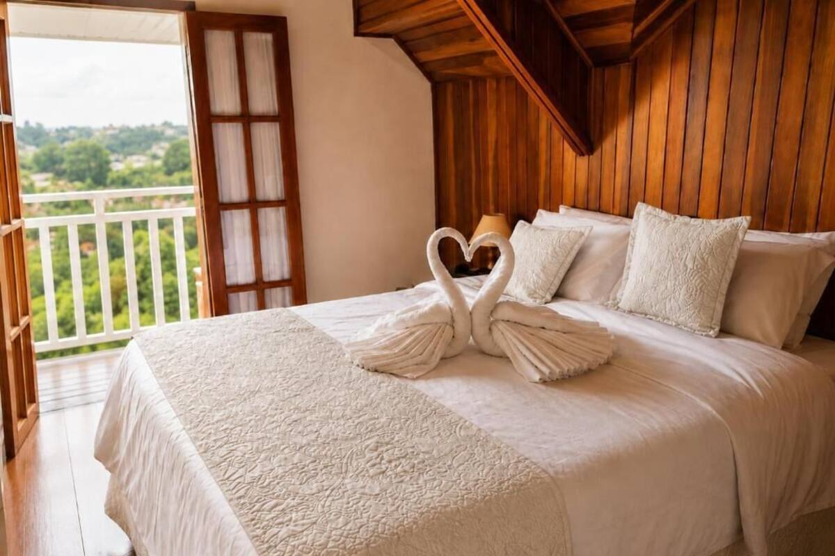 Ein Bett mit weißer Bettdecke und Kissen, eine Holzbalkendecke und Blick ins Grüne.