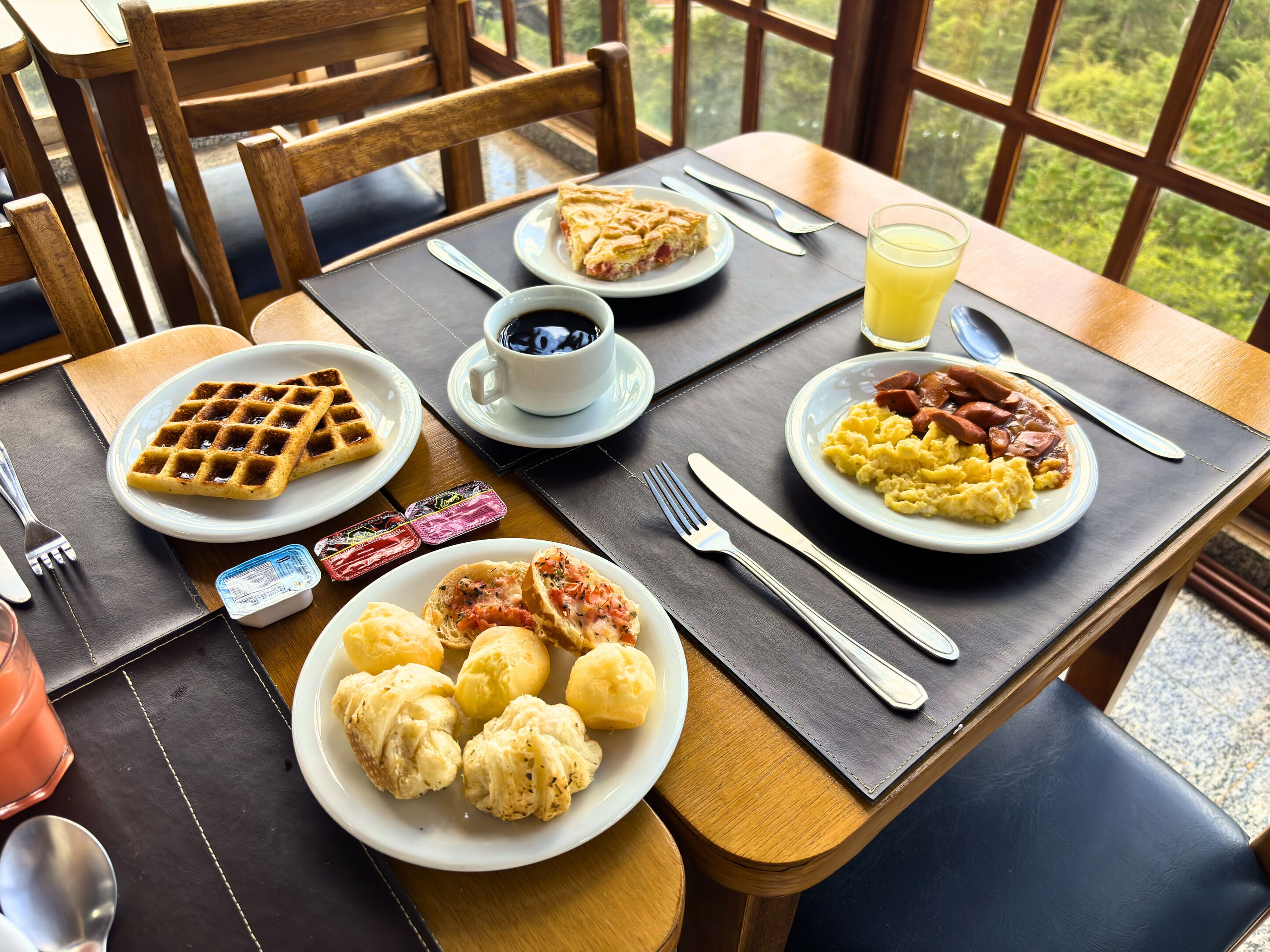 Ein Frühstückstisch mit Waffeln, Rührei, Würstchen und einem Glas Orangensaft.