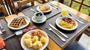 Ein Frühstückstisch mit Waffeln, Rührei, Würstchen und einem Glas Orangensaft.