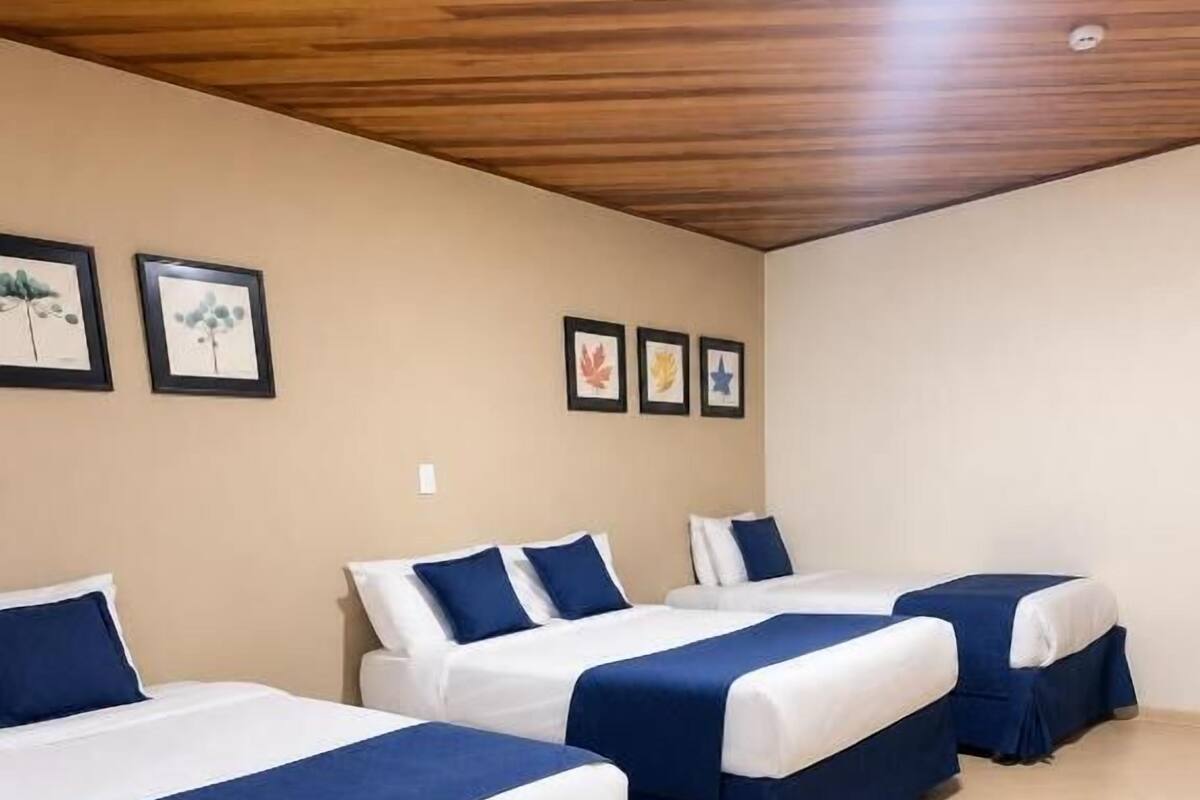 Ein Hotelzimmer mit drei Betten, Holzboden und gerahmten Bildern an der Wand.