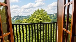 An open balcony with a stone floor, a black metal railing, and a view of green trees and hills. - Pousada Chateau Elegance (Campos do Jordão)
