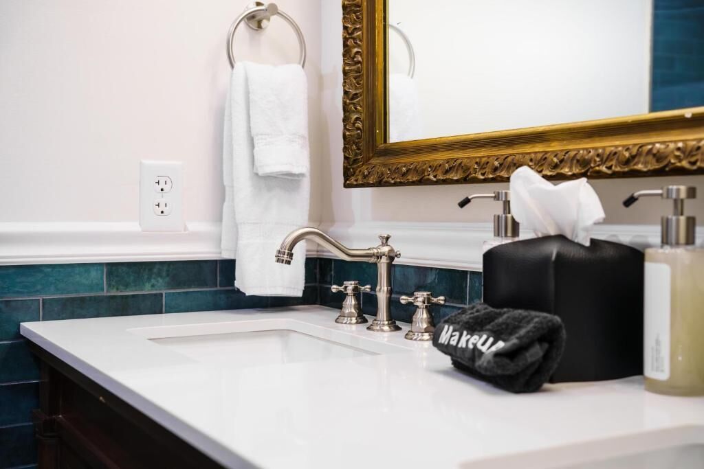 A bathroom with a white sink, a gold-framed mirror, a towel rack with a white towel, and a black towel on the counter.