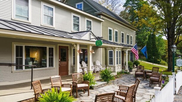 A two-story building with a porch, outdoor seating, and flags. - Green Trails Inn (Brookfield)