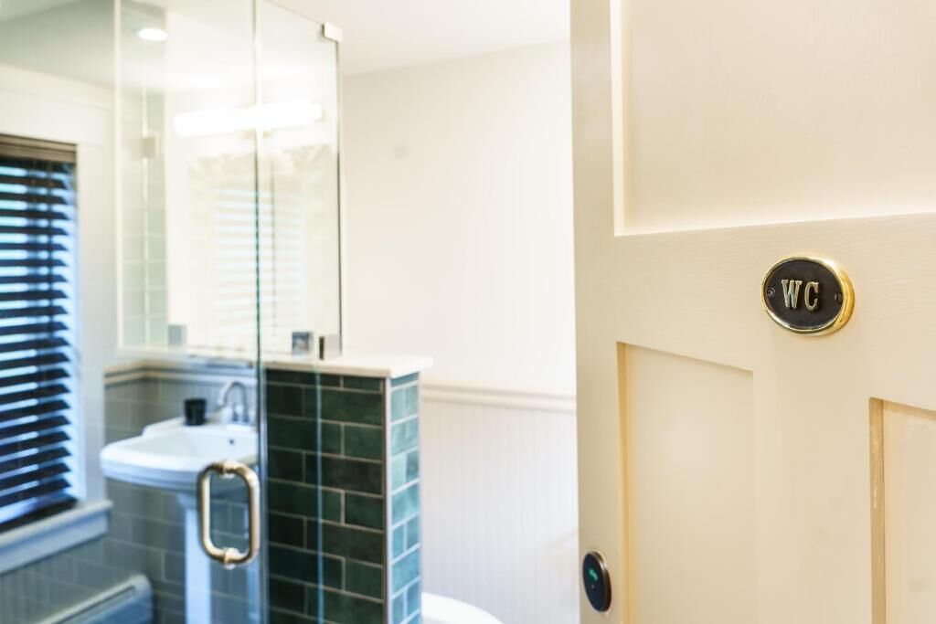 Un baño con cabina de ducha de vidrio, un lavabo con pomo dorado y un letrero de inodoro en la puerta.