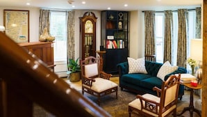 A cozy living room with a green sofa, wooden chairs, a bookshelf, and a large clock. - Green Trails Inn (Brookfield)