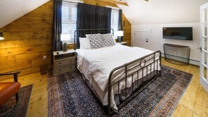 A bedroom with a sloped ceiling, a bed with a metal frame, a patterned rug, a wooden wall, a television, and a chair. - Green Trails Inn (Brookfield)