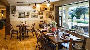 A dining area with wooden tables and chairs, a view of the outdoors through large windows, and various framed pictures on the walls. - Green Trails Inn (Brookfield)