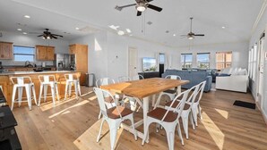 A spacious kitchen with wooden cabinets, a dining area with a wooden table and white chairs, and a living area with a sofa and a TV.
