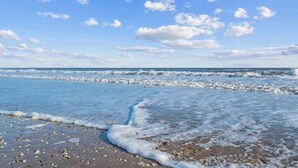A beach with waves, pebbles, and a clear sky.