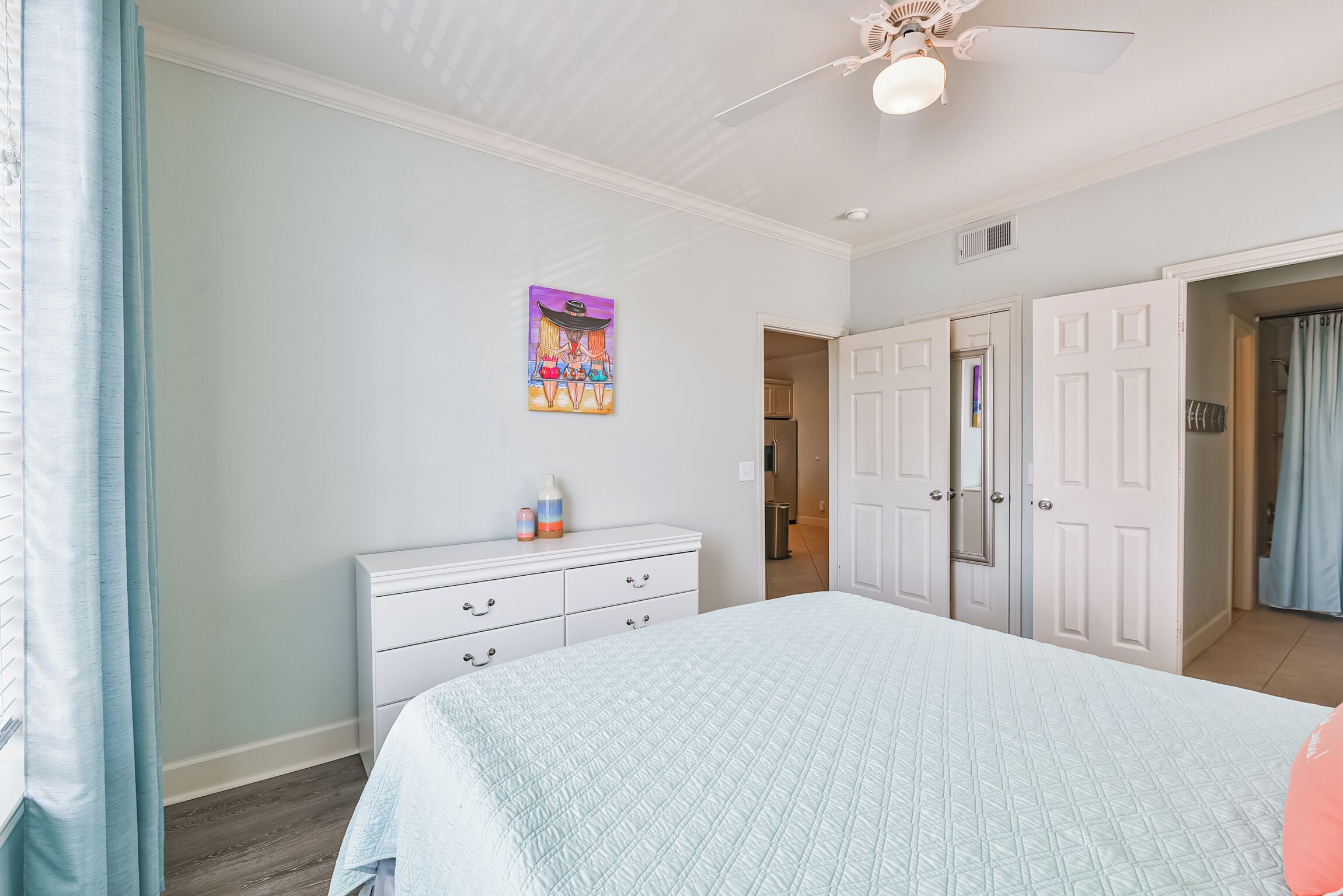 A bedroom with a bed, a dresser, a ceiling fan, and a door leading to another room.
