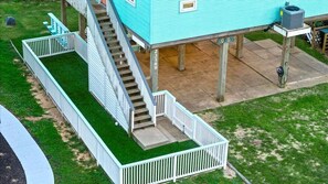 Elevated home design with exterior stairs and a fenced yard, offering a safe and convenient outdoor space for families. - Beachfront + Hot Tub | Putt-Putt | Pet-Friendly (Galveston)