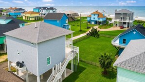 A coastal residential area with houses, a clear sky, and a view of the ocean. - Walk to Beach with Expansive Deck & Hot Tub | Sleeps 12 (Port Bolivar)
