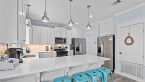 A modern kitchen with white cabinets, stainless steel appliances, and blue bar stools. - Walk to Beach with Expansive Deck & Hot Tub | Sleeps 12 (Port Bolivar)