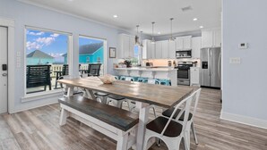 A modern kitchen with white cabinets, stainless steel appliances, and a wooden dining table with chairs. - Walk to Beach with Expansive Deck & Hot Tub | Sleeps 12 (Port Bolivar)