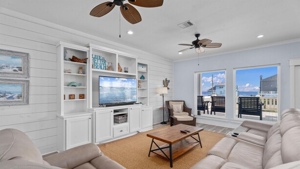 A living room with a sofa, a coffee table, a TV, and a ceiling fan. - Walk to Beach with Expansive Deck & Hot Tub | Sleeps 12 (Port Bolivar)