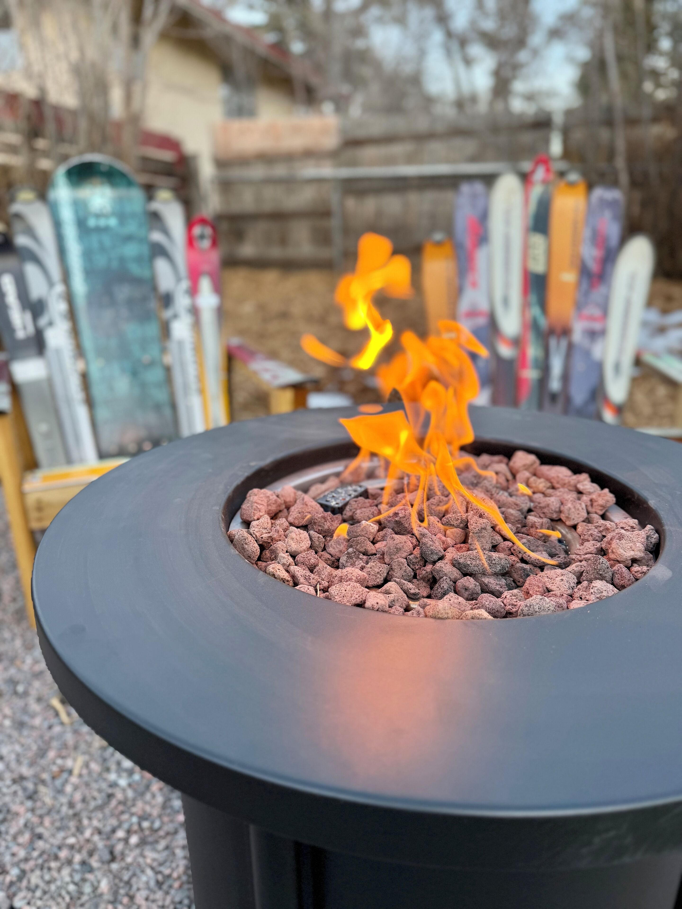 A circular outdoor fire pit with a black rim and a central fire.