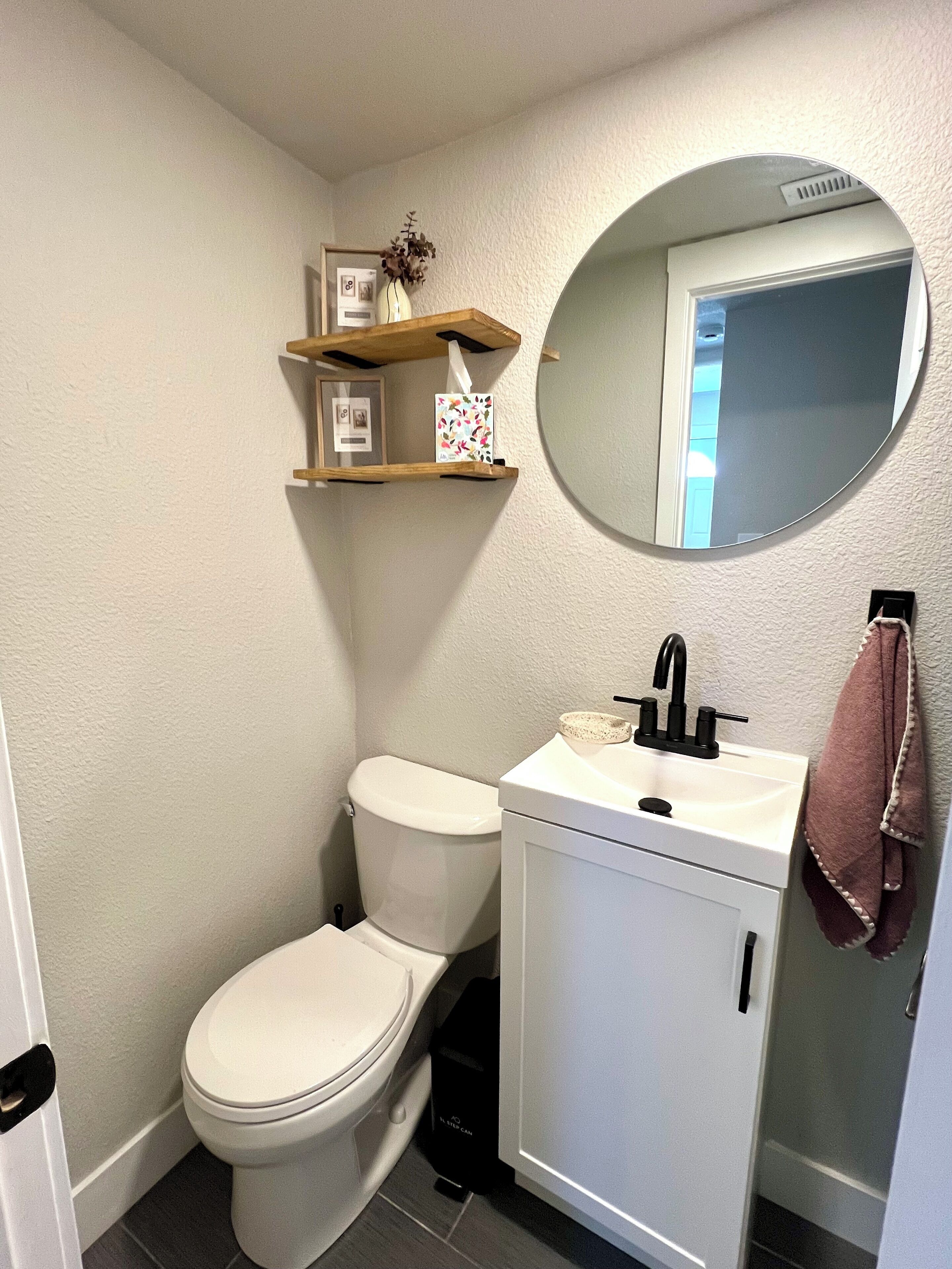 A bathroom with a toilet, sink, mirror, and a shelf with decorative items.