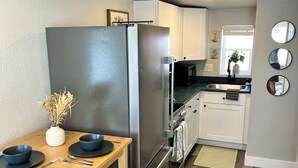Eine kleine Küche mit Edelstahl-Kühlschrank, Holztisch und weißen Schränken.