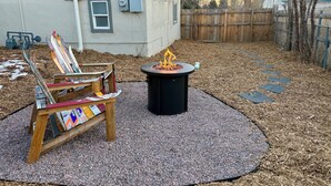 Ein Garten mit einem Feuerkorb, einem Holzstuhl und einem Metallstuhl mit Skiern.