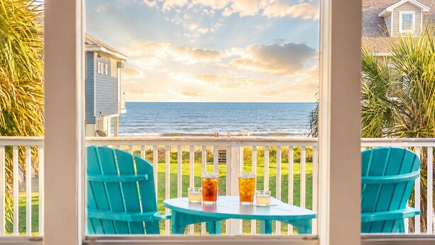 A view from a balcony with a table and chairs, overlooking a body of water and a grassy area. - Beachview | Fire Pit | Cargo Lift | Pet-Friendly | Steps to Shore (Galveston)