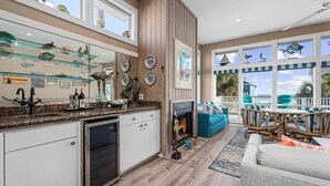 A spacious living area with a fireplace, a dining table with chairs, and a view of the outdoors. - Beachview | Fire Pit | Cargo Lift | Pet-Friendly | Steps to Shore (Galveston)