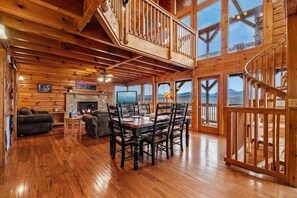 A spacious wooden cabin with a dining area, fireplace, and large windows offering mountain views. - Smoky Mountain Views | Hot Tub | Game Room | Sleeps 12 (Sevierville)