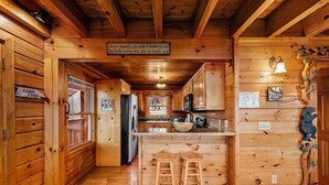 Interior de una cabaña con paredes de madera, una zona de cocina y una barra con taburetes.