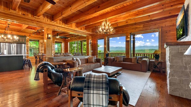 A spacious wooden cabin interior with a dining area, seating, and a fireplace. - Luxury 12BR Lodge Sleeps 60 | Heated Pool + Pickleball Court + Sauna + Putt Putt (Sevierville)