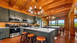 A spacious kitchen with wooden ceilings, stainless steel appliances, and a large island with stools. - Luxury 12BR Lodge Sleeps 60 | Heated Pool + Pickleball Court + Sauna + Putt Putt (Sevierville)
