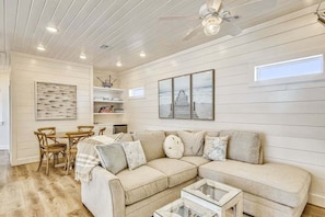 A spacious living room with a large beige sectional sofa, a glass coffee table, and a dining area with wooden chairs and a white table. - Luxury 5BR Beachfront Home | Sleeps 14 | Community Pool (Galveston)