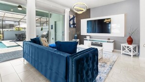 A modern living room with a large TV, a blue sofa, and a glass door leading to a balcony. - Chic Family Home, Mario Bros, Harry Potter & Pool (Davenport)