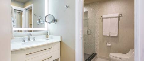 A modern bathroom with a large mirror, two sinks, a toilet, and a shower area.