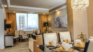 Habitación de hotel con zona de comedor, sofá, candelabro y vistas a la ciudad.