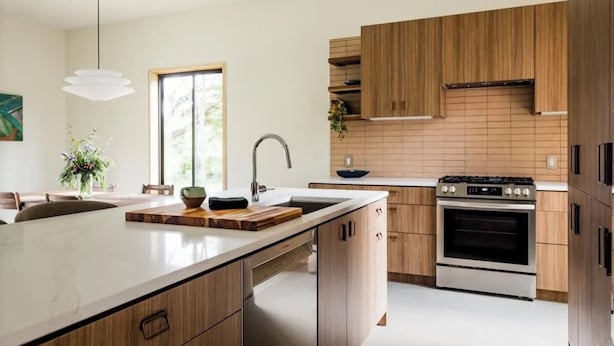 Eine moderne Küche mit Holzschränken, einer großen Kochinsel, einem eingebauten Backofen und einer Pendelleuchte.