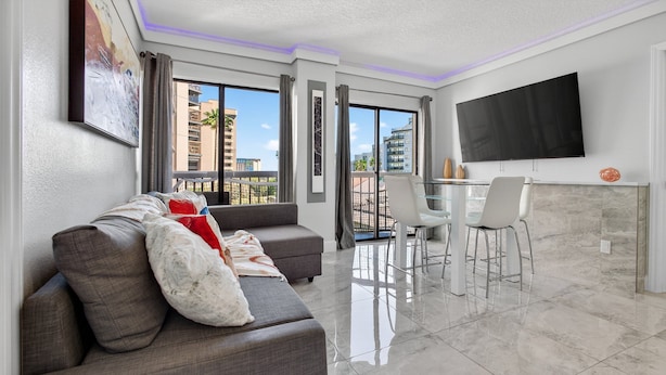 A modern living room with a grey sofa, a flat-screen TV, and a dining area with a glass table and chairs. - 6165 CD Unit 3302 Enclave Urban Escape (Orlando)