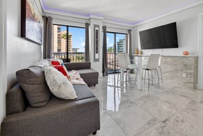 A modern living room with a grey sofa, a flat-screen TV, and a dining area with a glass table and chairs. - 6165 CD Unit 3302 Enclave Urban Escape (Orlando)