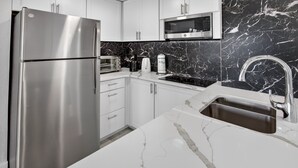 A modern kitchen with a stainless steel refrigerator, a microwave, a sink with a faucet, and a marble countertop. - 6165 CD Unit 3302 Enclave Urban Escape (Orlando)