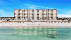 Un hotel grande con varios pisos y balcones, ubicado junto a una playa de aguas claras y orilla arenosa.