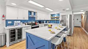 Cocina moderna con armarios blancos, salpicadero azul, electrodomésticos de acero inoxidable y una isla central con taburetes de bar.