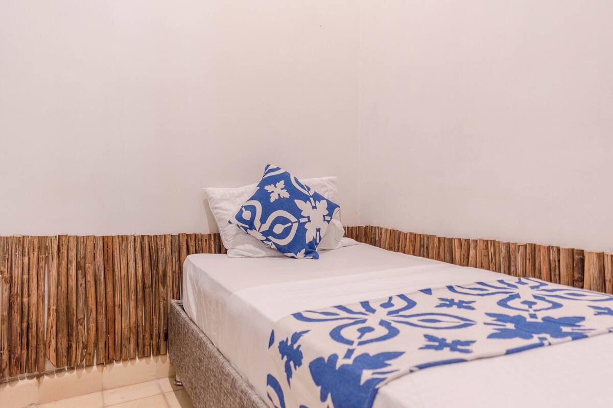 Una cama individual con una colcha estampada y una almohada azul con diseño blanco.