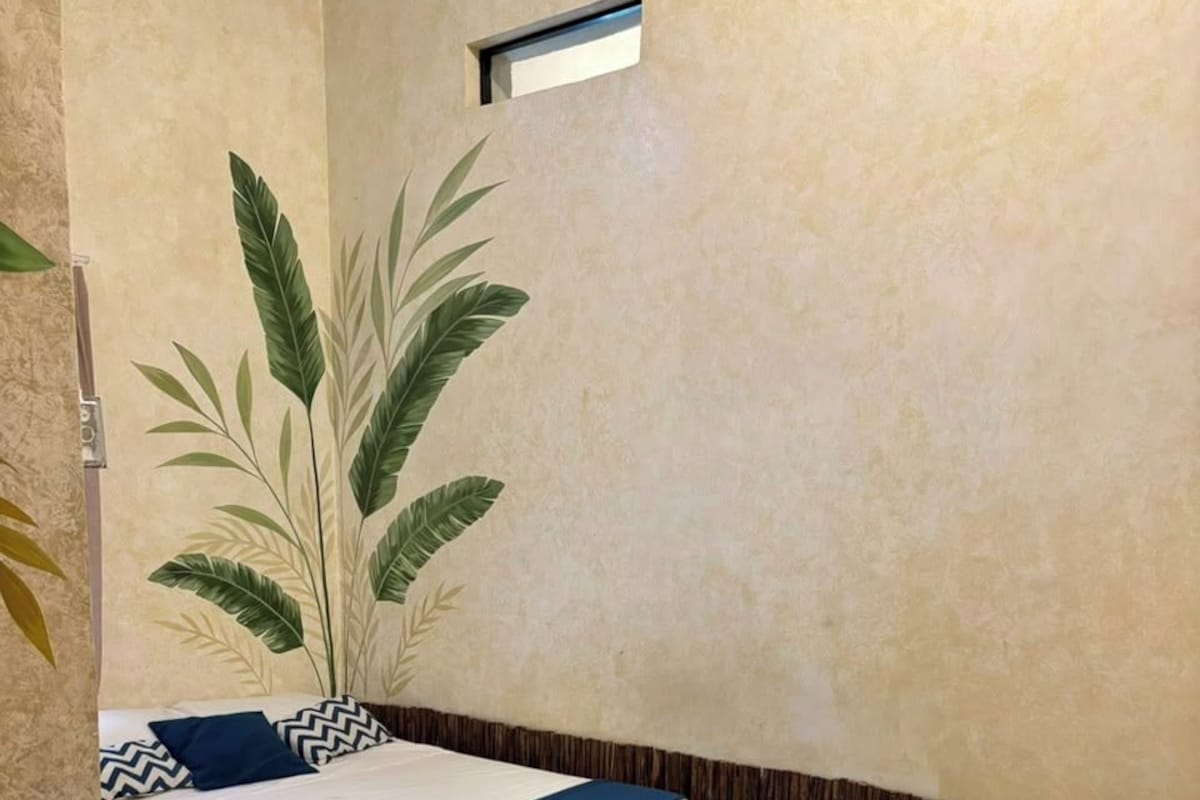 Habitación de hotel con dos camas, una planta grande en maceta y un ventanal pequeño.