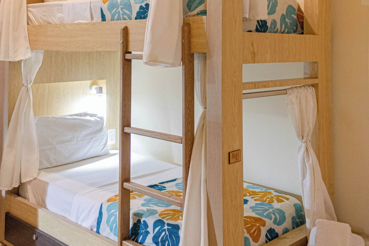 Una cama individual con cortinas, cabecera de madera y mesita de noche con una toalla.