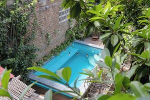 Una piscina rectangular rodeada de abundante vegetación y un muro de ladrillo.