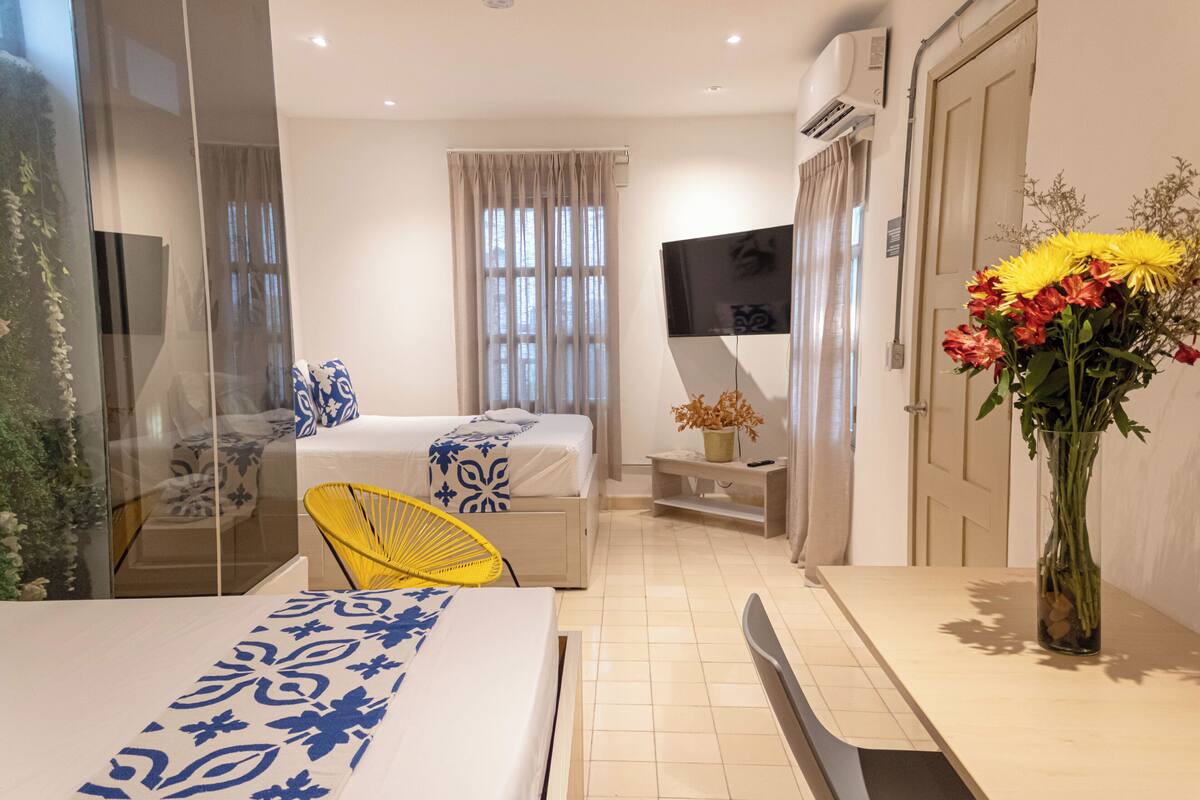 Una habitación de hotel moderna con una cama, un escritorio, una silla, un televisor y un jarrón con flores.