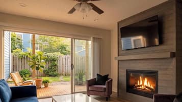 A living room with a fireplace, a TV mounted above it, and a sliding glass door leading to a patio with outdoor furniture.
