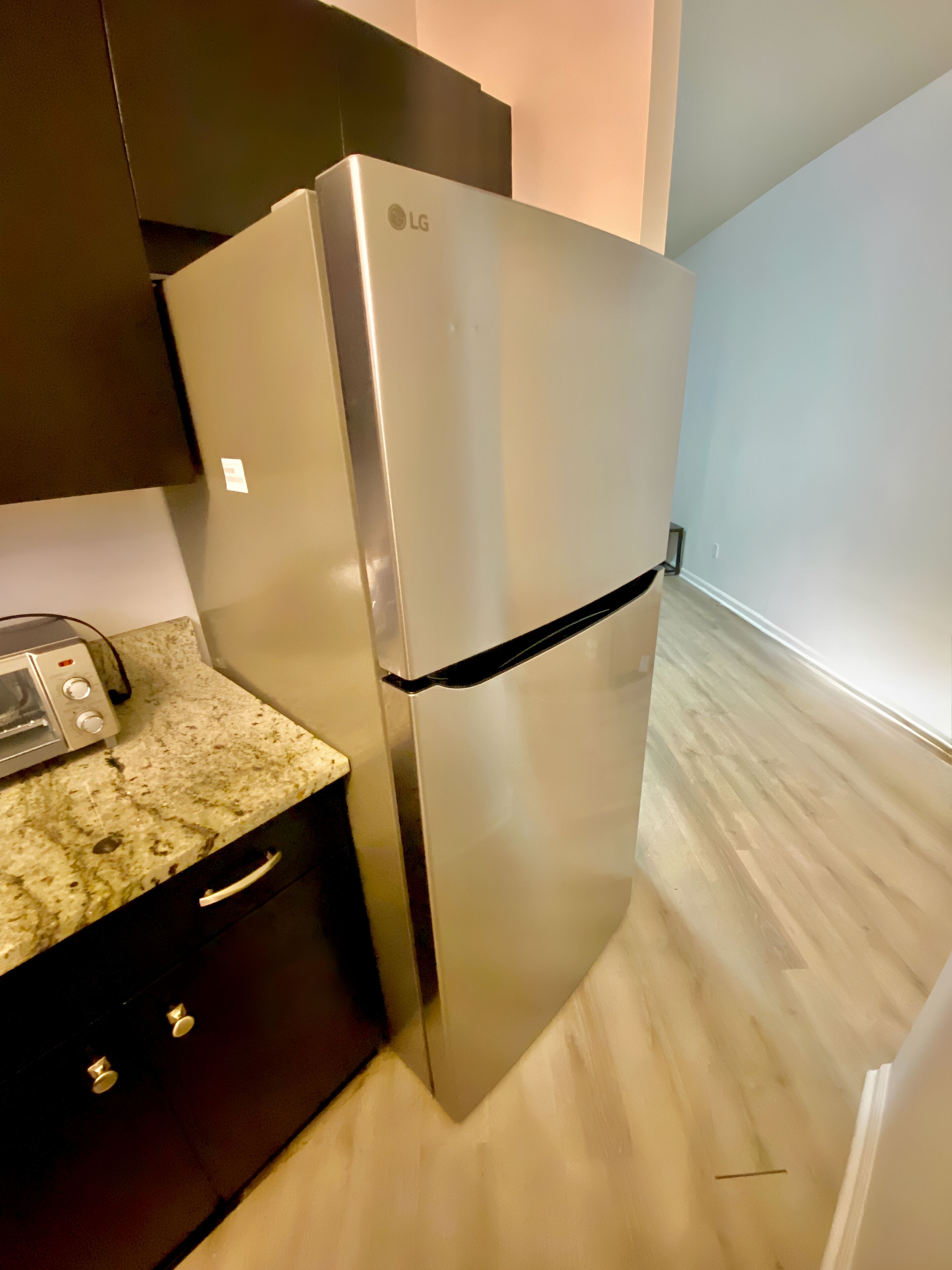 A stainless steel LG refrigerator in a kitchen with a granite countertop, dark cabinetry, and a light wooden floor.
